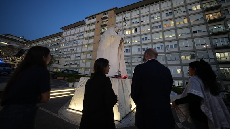Varias personas se reúnen para rezar por el papa León XIV junto a una estatua del San Juan...